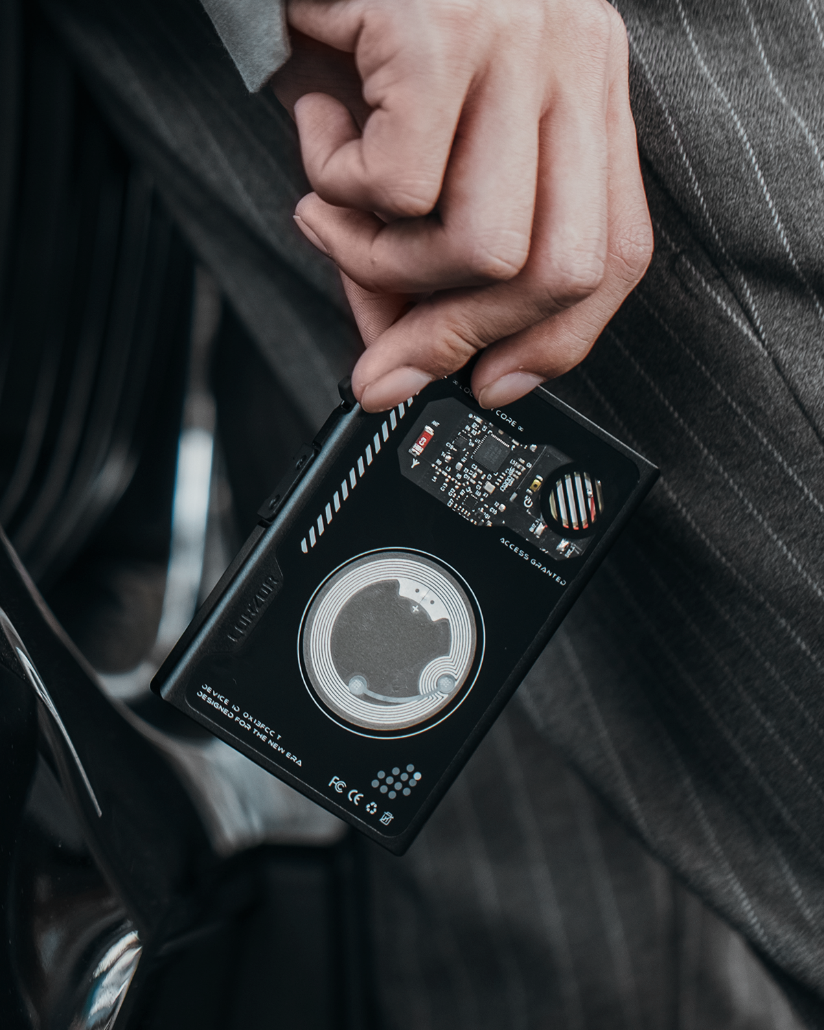 Hand holding a black slim wallet showing an exposed internal coil and electronic board through the back panel.