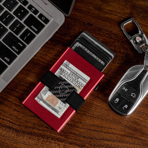 Red aluminum card wallet on a wooden desk holding cash and cards