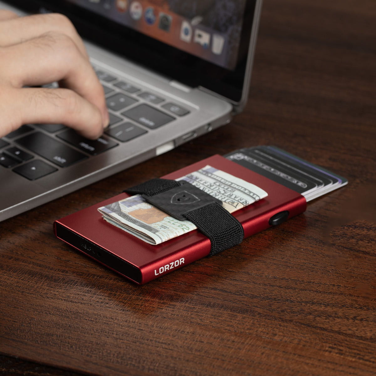 Red aluminum RFID wallet on a desk with cards extended and cash held by a black strap
